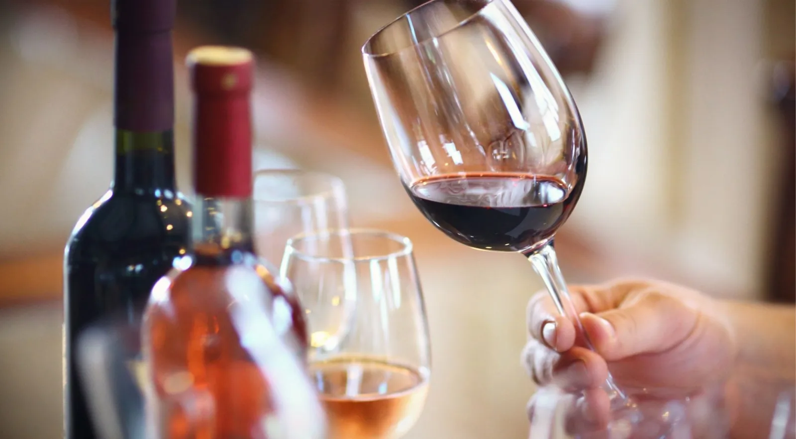 A hand swirling a glass of red wine beside open bottles of red and rosé at a tasting counter