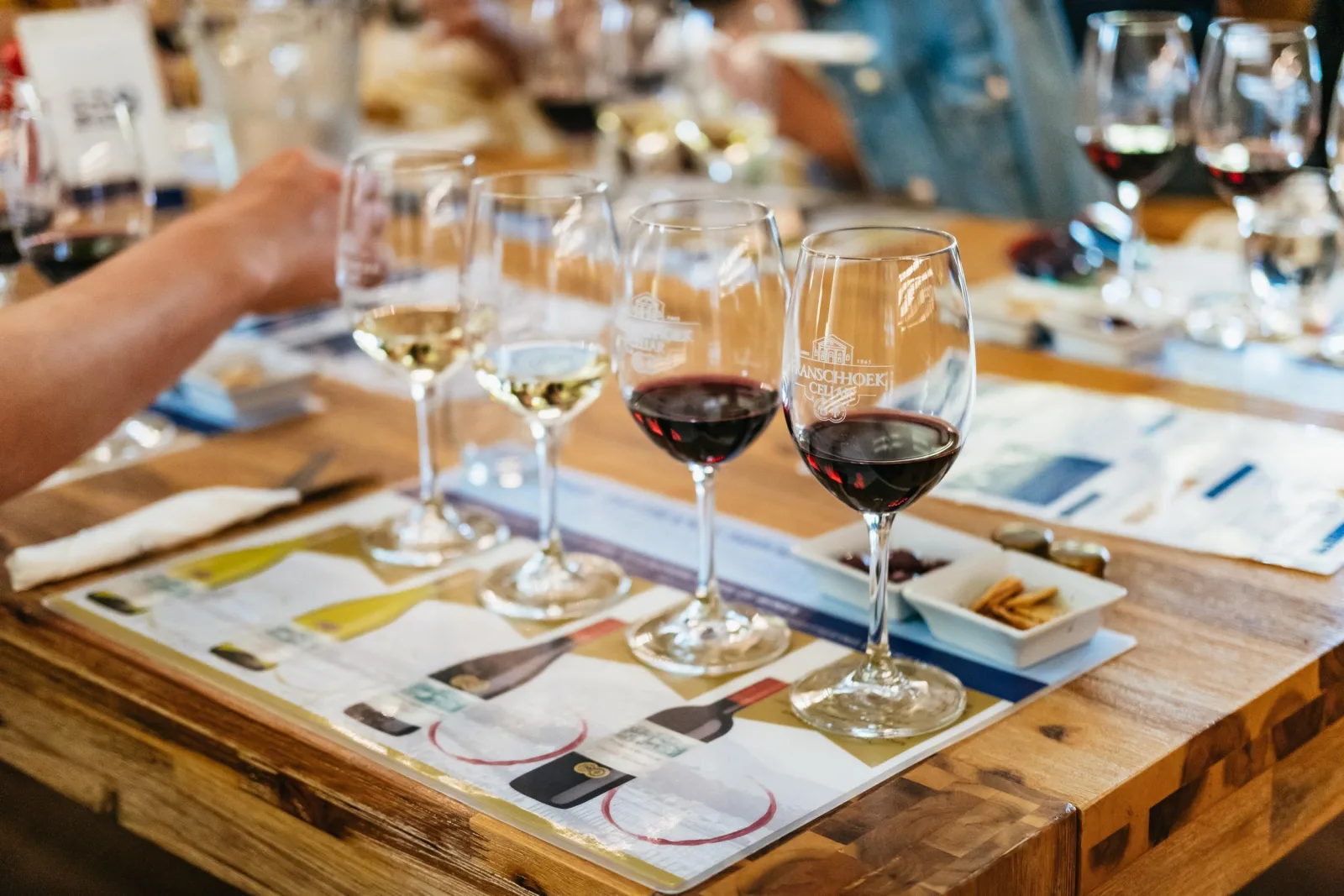 A row of white and red tasting glasses on a wooden table with tasting notes and snacks