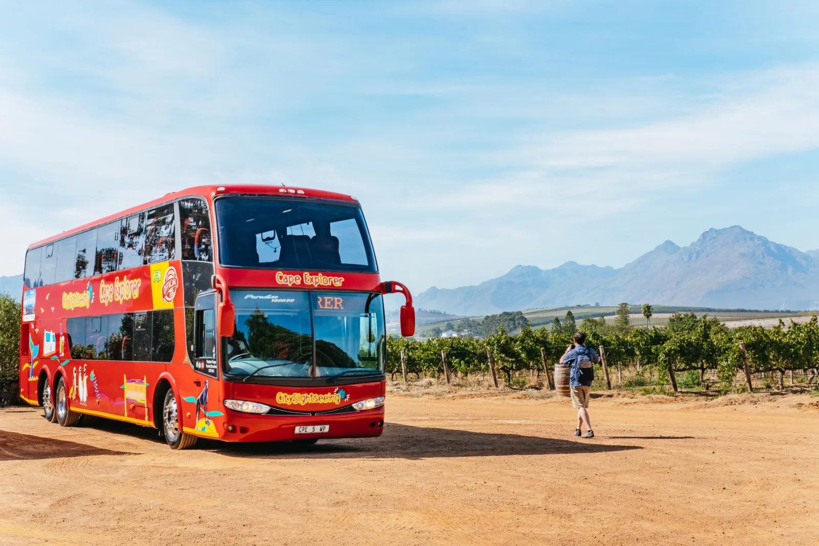 A red City Sightseeing double-decker parked at a Cape Winelands vineyard with the mountains behind