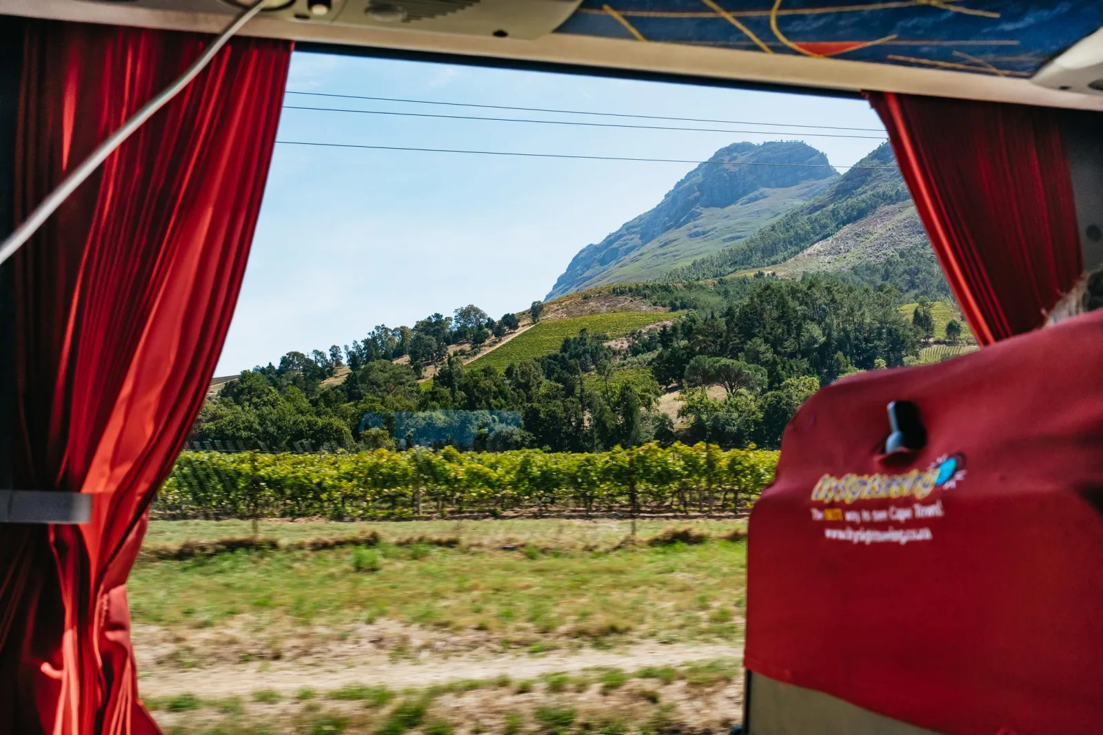 Vineyards and mountains seen through the curtained window of the tour coach