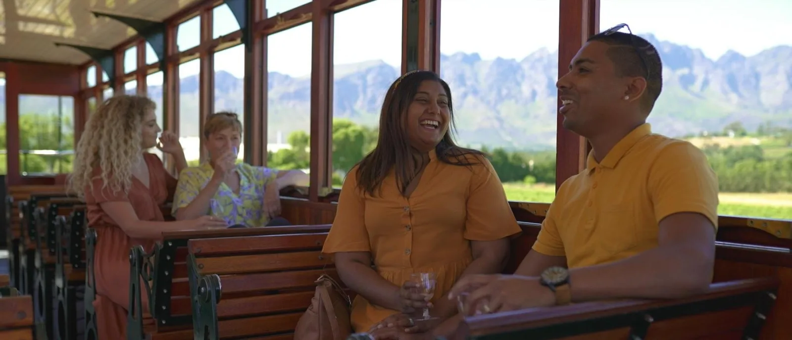 Passengers on the open wooden benches of the wine tram with the valley behind them