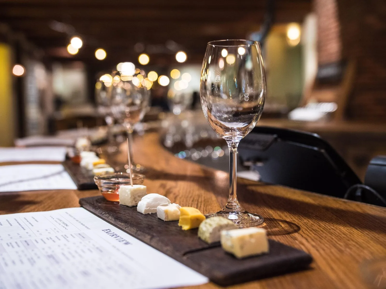 Glasses and a cheese board on a dark wooden counter in a candlelit tasting room