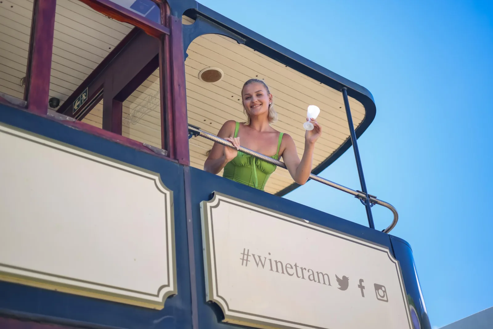 A guest on the upper deck of the wine tram beside the tram's own sign