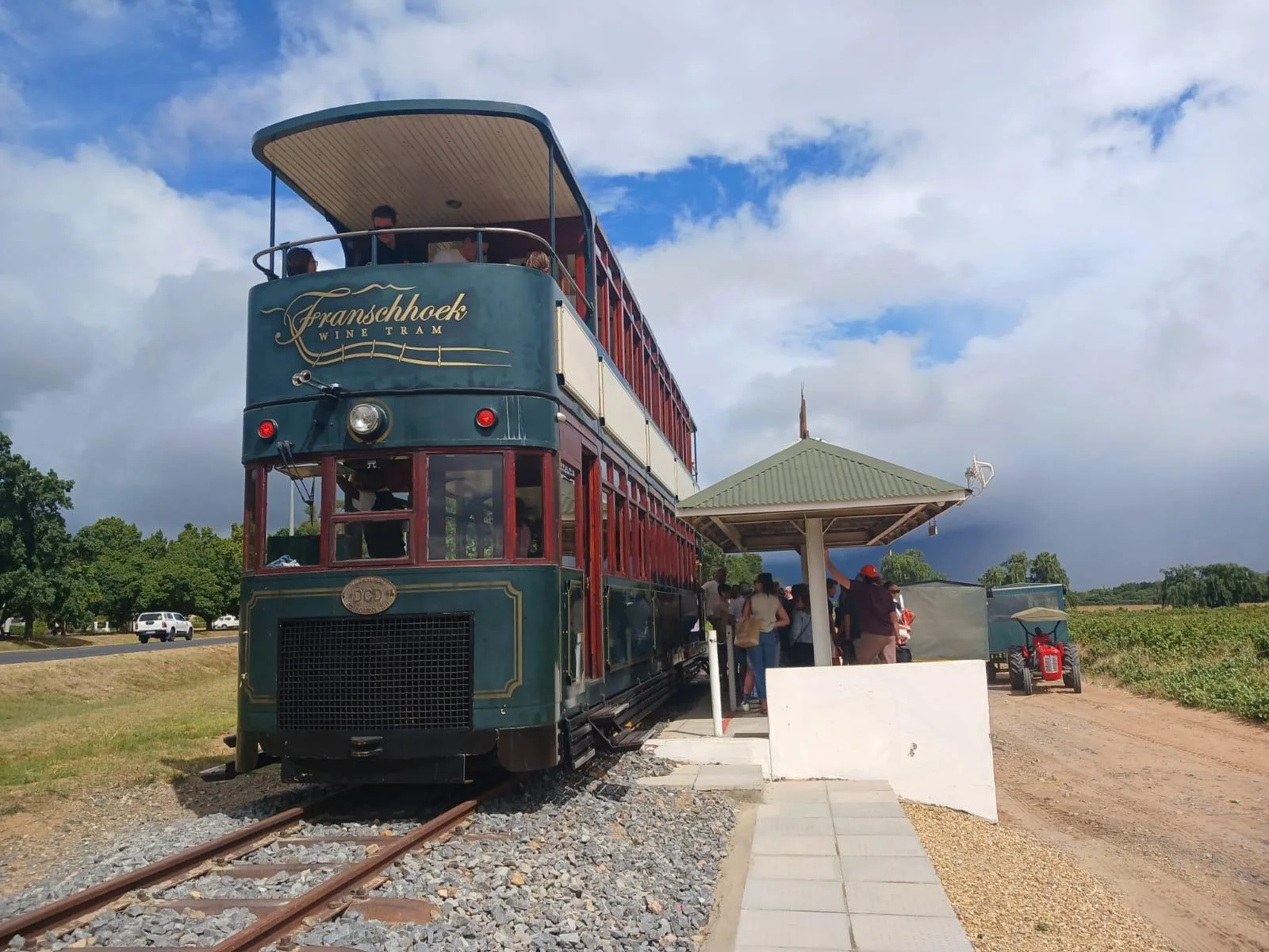 The Franschhoek Wine Tram at its trackside platform, seen wide with the shelter and the vineyards behind