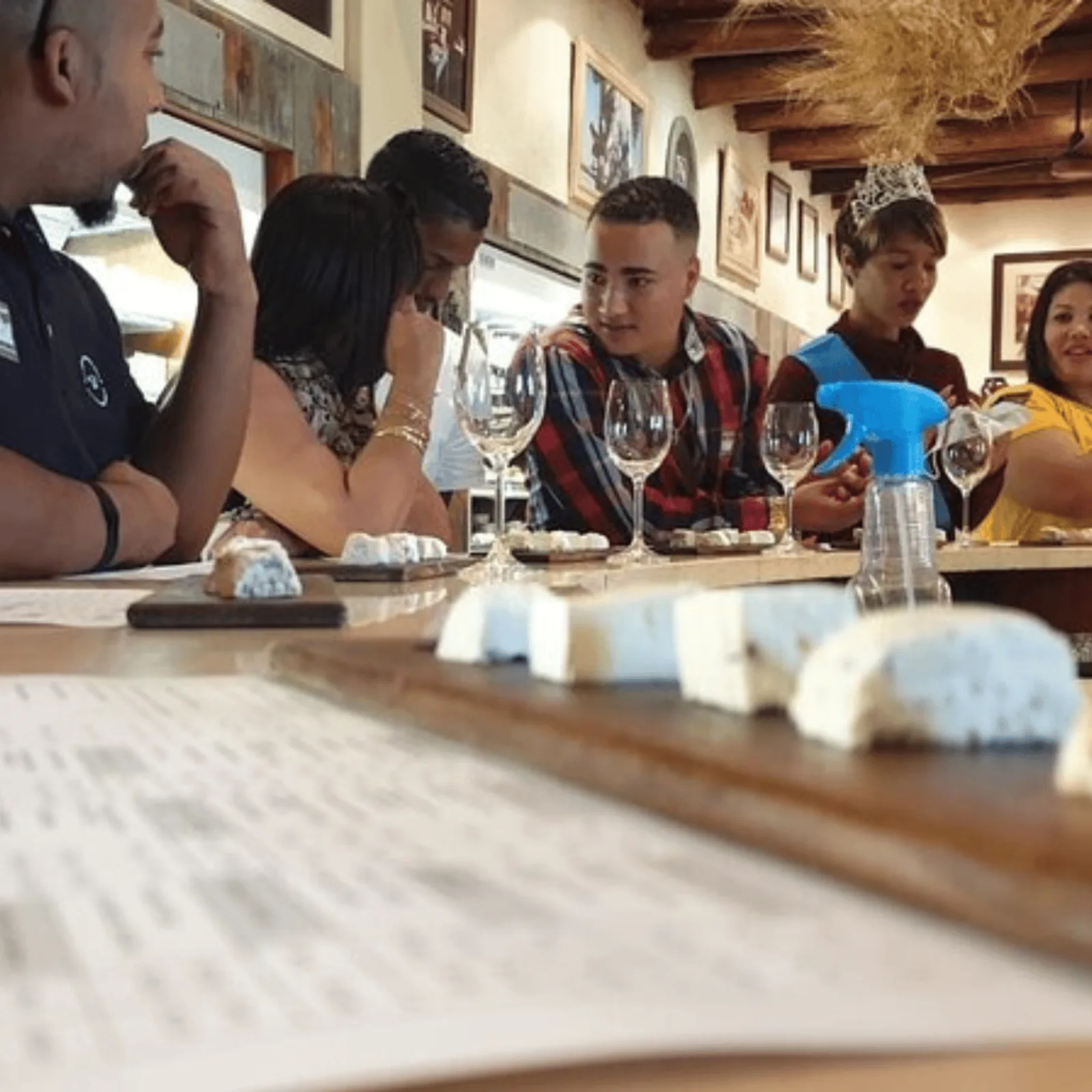 Guests seated along a tasting counter with a cheese board and a row of glasses