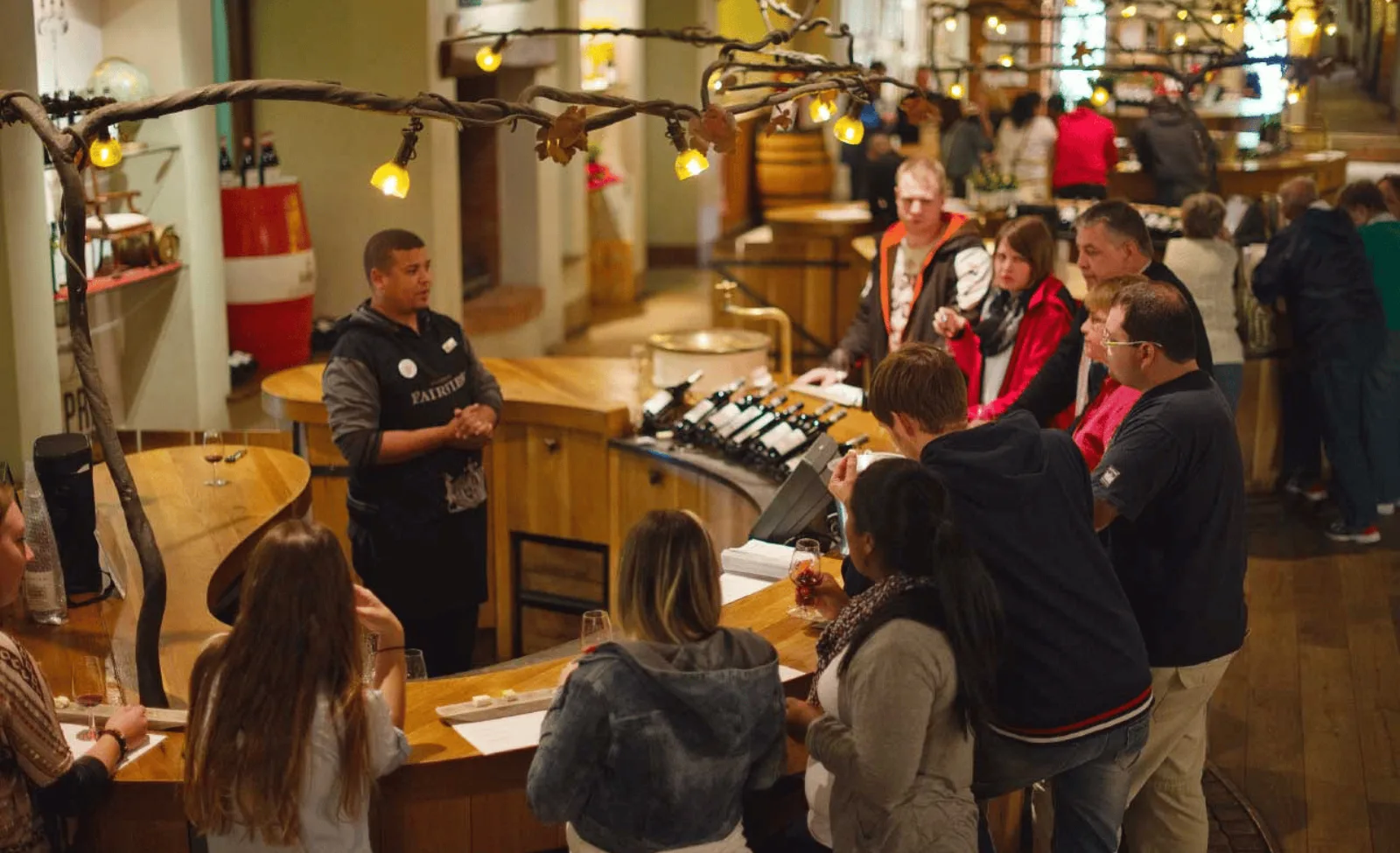 Guests around a busy estate tasting bar hung with lights and bottles